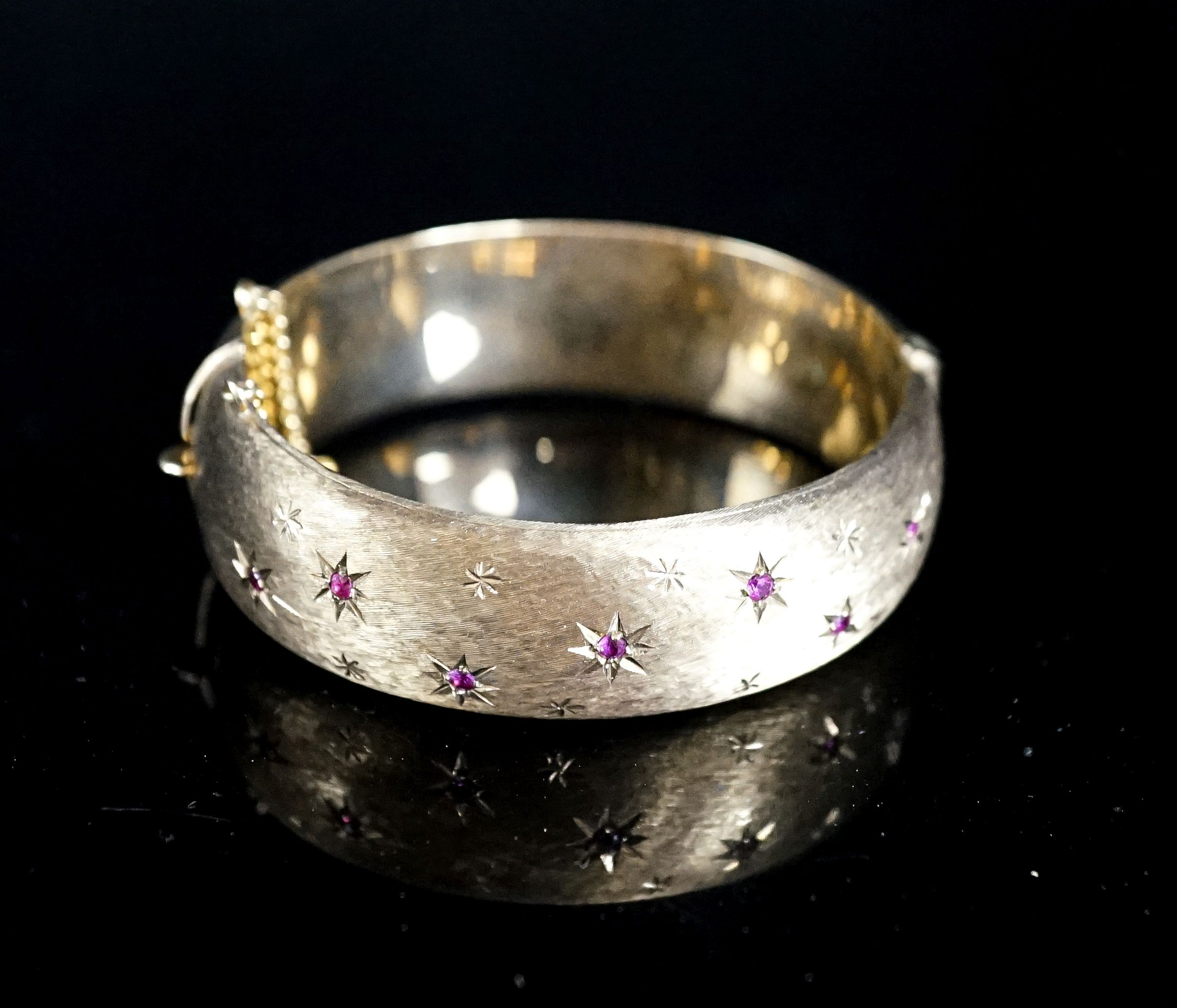 A 1960's engraved 9ct gold and ruby set hinged bracelet, interior diameter 58mm, gross weight 35.7 grams.